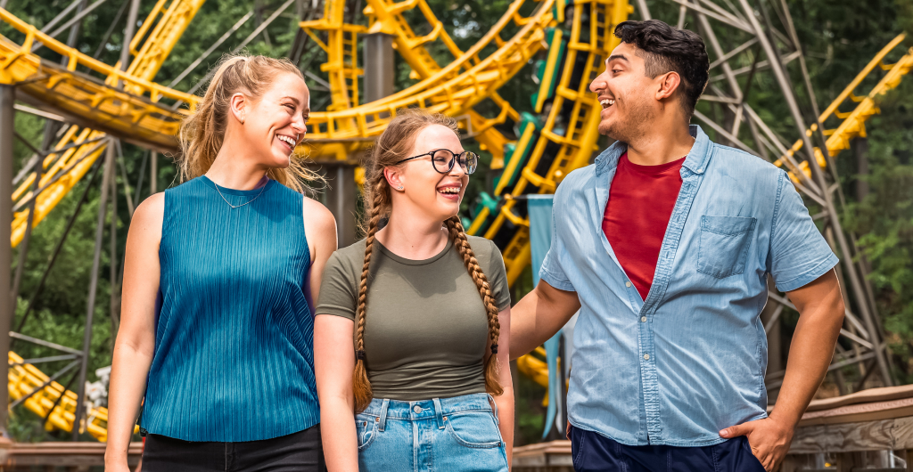 Three young adults in front of a roller coaster