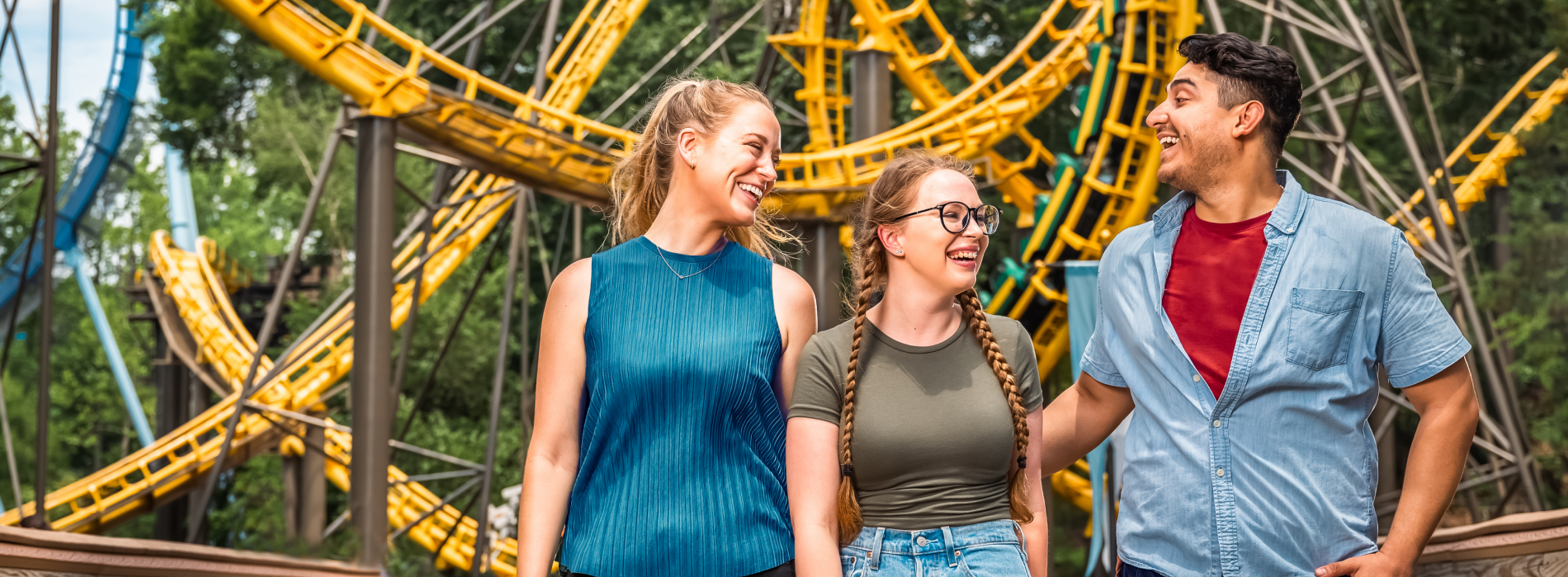 Three young adults in front of a roller coaster